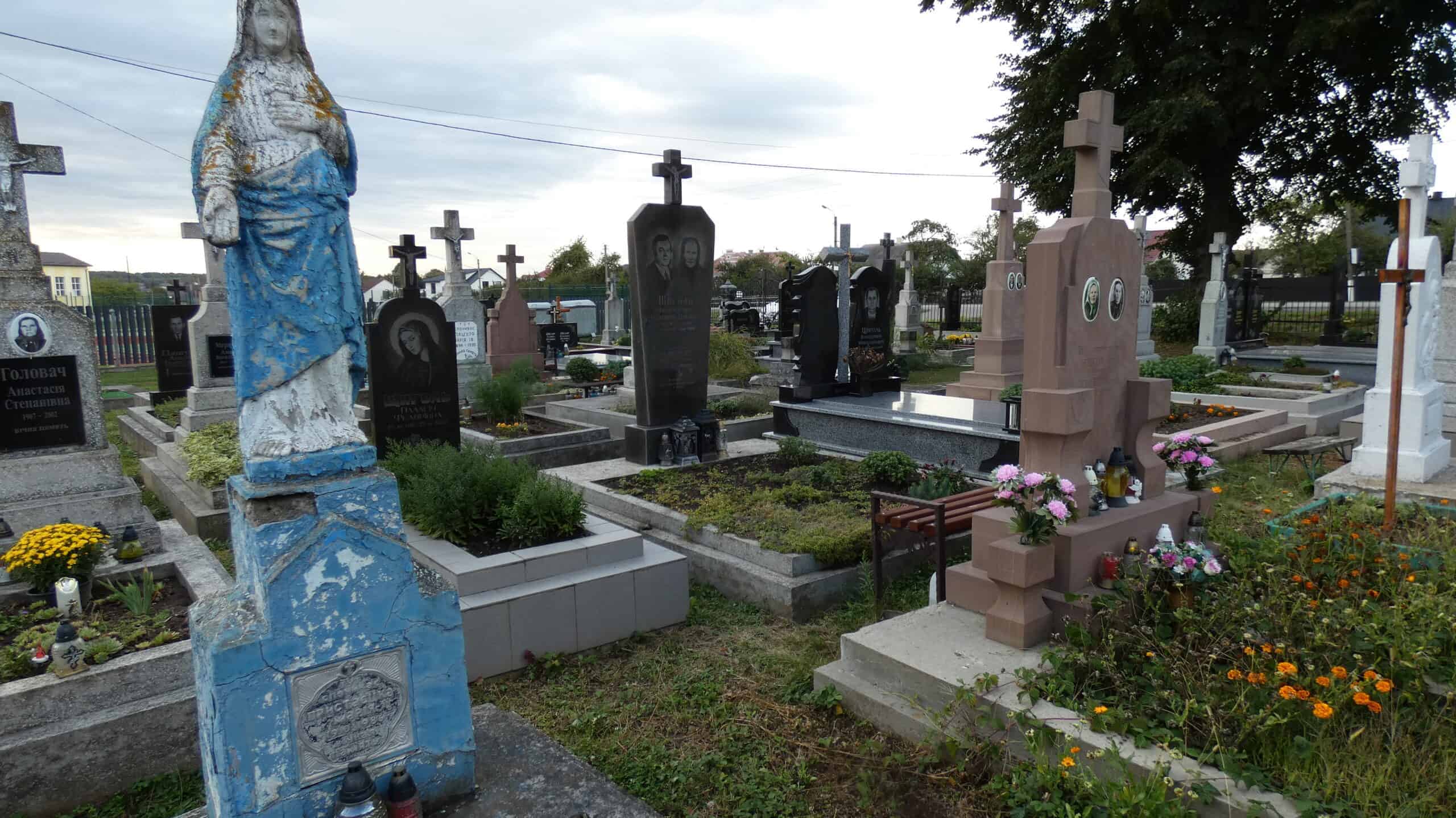 Вигляд цвинтаря в Бучачі з різноманітними пам’ятниками та квітами, спокійна атмосфера для поминання.
