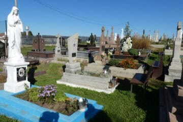 Вигляд цвинтаря в Буцачі з різноманітними могилами і скульптурами в сонячну погоду.