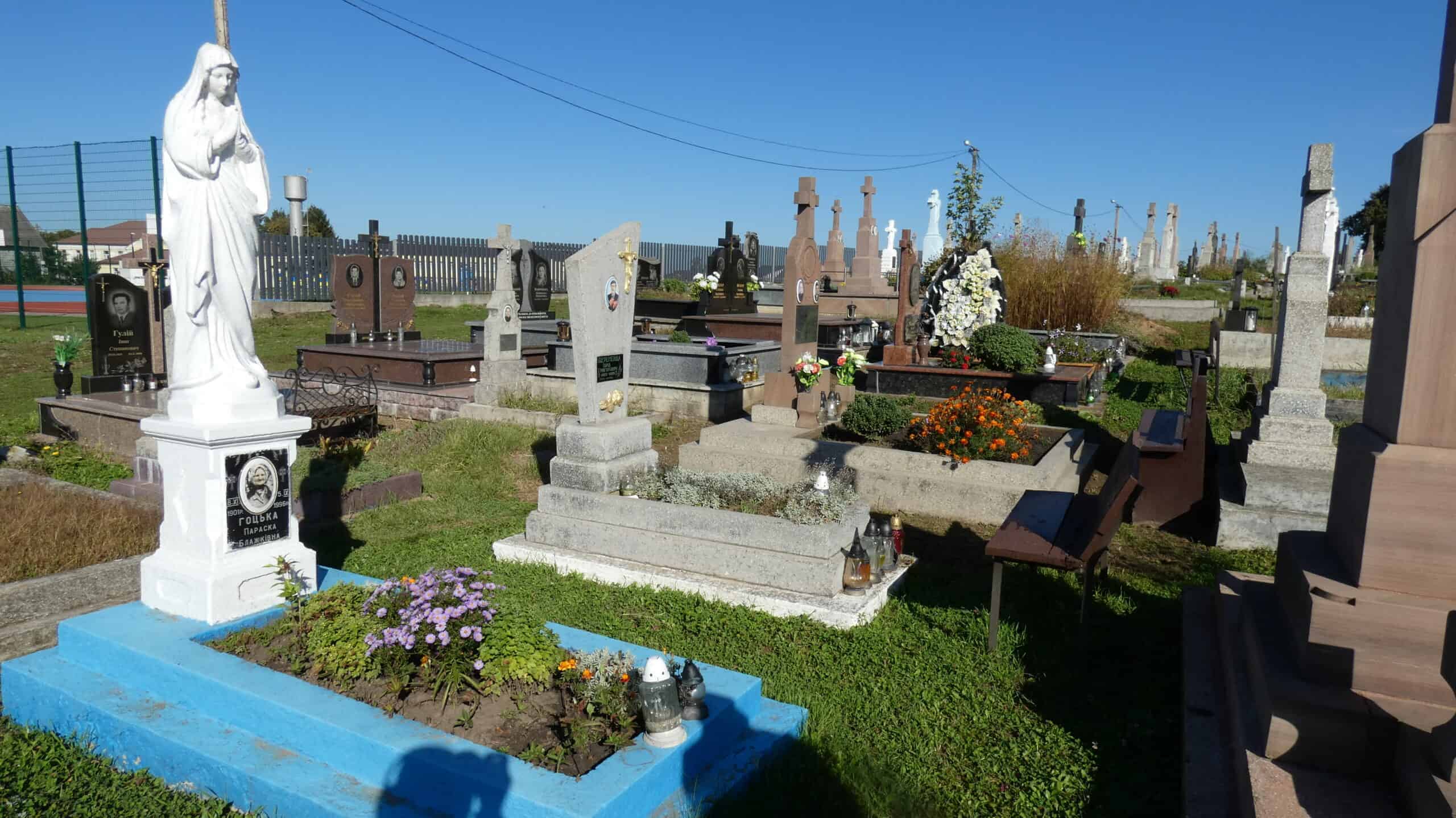 Вигляд цвинтаря в Буцачі з різноманітними могилами і скульптурами в сонячну погоду.