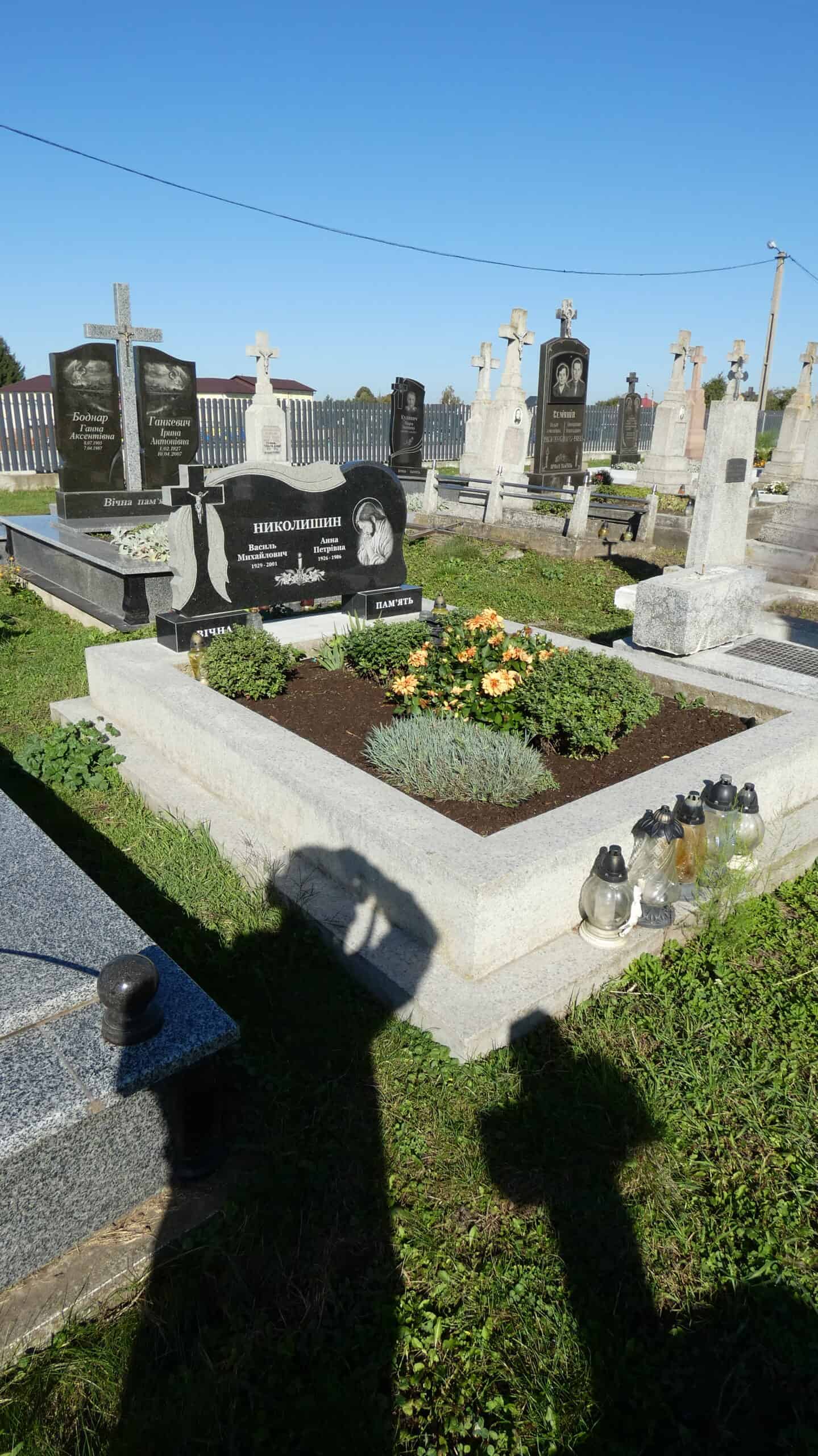 Меморіальний чорний пам’ятник на цвинтарі у Буцазі, могили з квітами та свічками, історичне кладовище України.