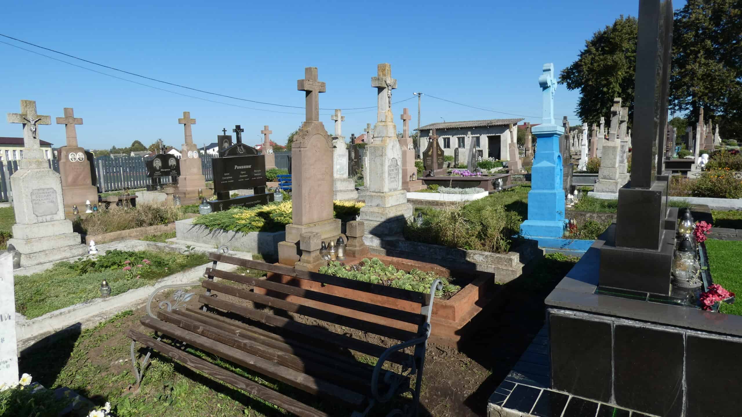 Могили на кладовищі в Буцкачу з хрестами та квітами, пам’ятники та лавки для відвідувачів.
