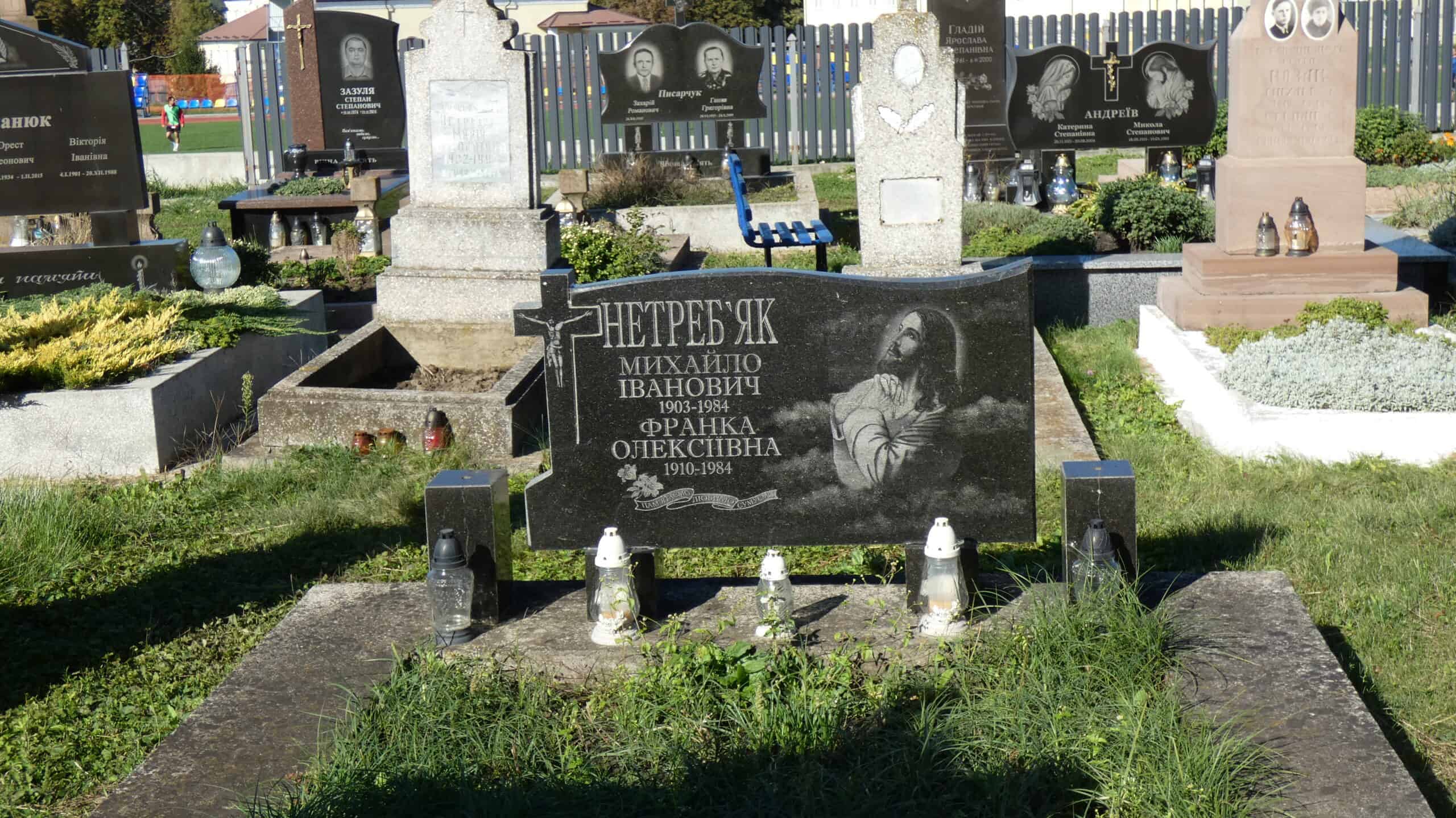 Меморіальний пам'ятник на цвинтарі Буцач, могила з написом і іконою Ісуса Христа, квіткові та свічкові прикраси.