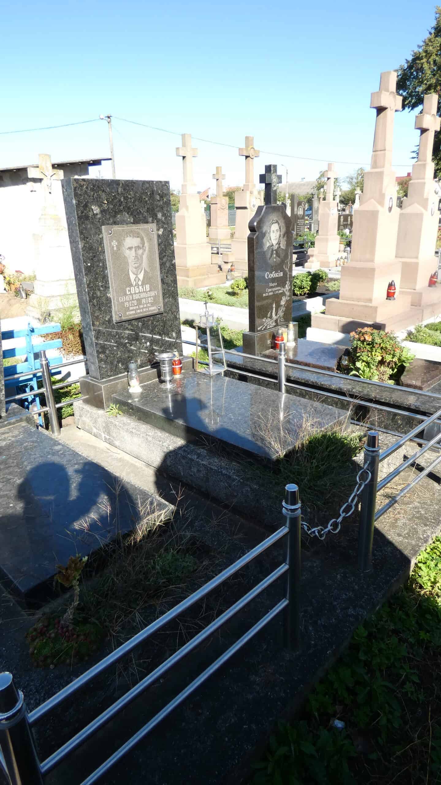 Могила на цвинтарі з чорним і сірим пам'ятником з фотографією та лампадами.