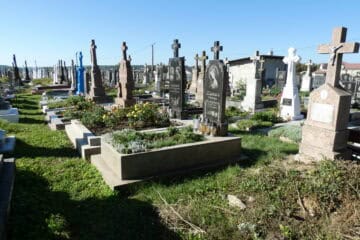 Могили на українському цвинтарі в Бучачі з пам'ятниками та квітами у сонячний день.