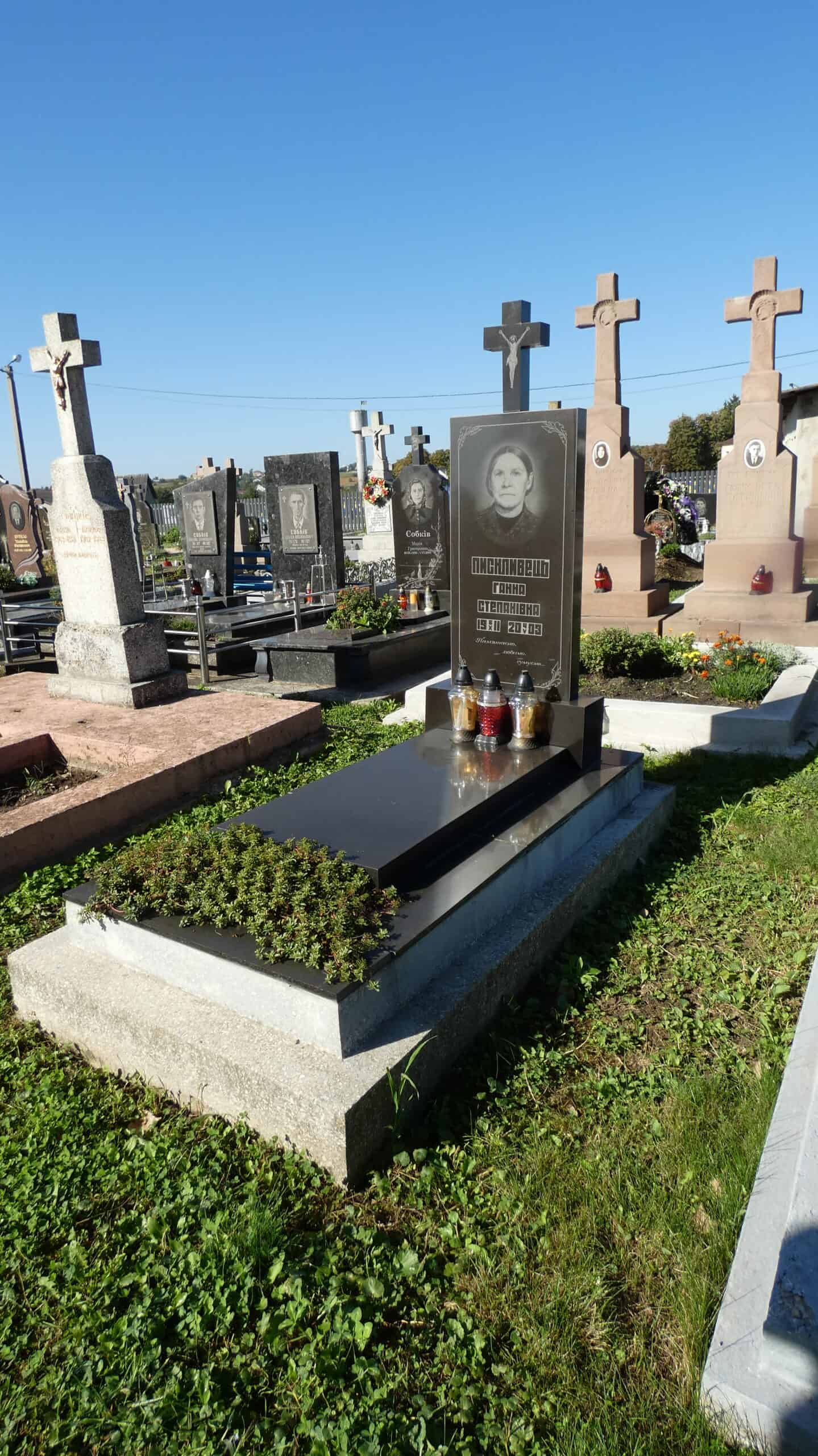 Меморіальний надгробок у цвинтарі Буцач, з чорним гранітним пам’ятником і квітами.