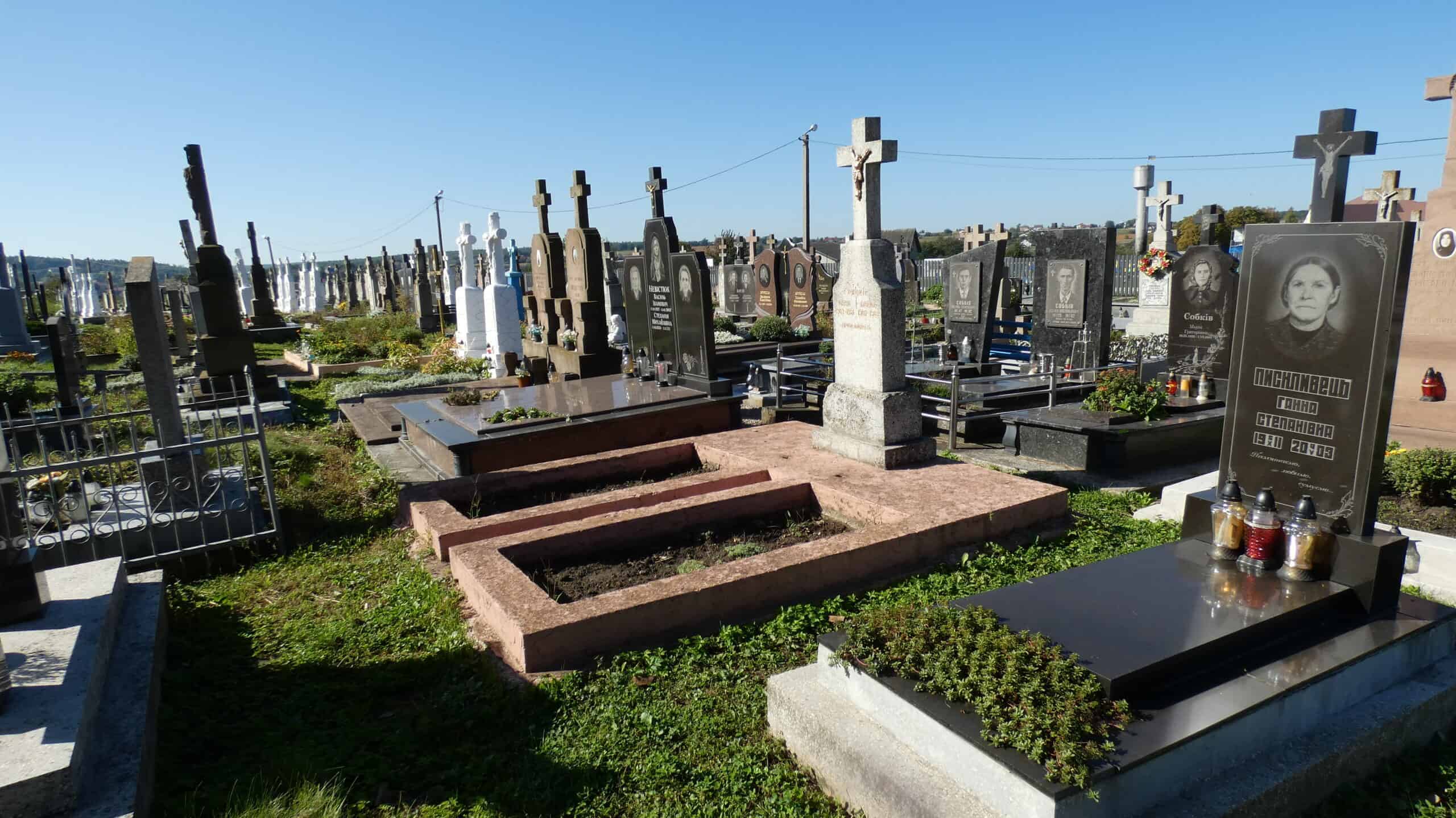 Могили на цвинтарі в Бучачі з пам'ятними плитами і хрестами, огляд у сонячну погоду.