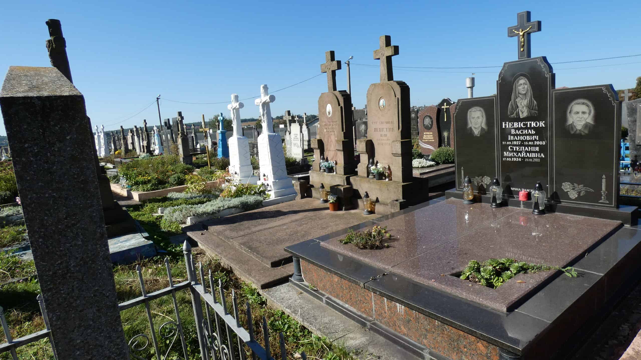 Меморіальні чорні гранітні надгробки з портретами та хрестами на цвинтарі Буцакіце.