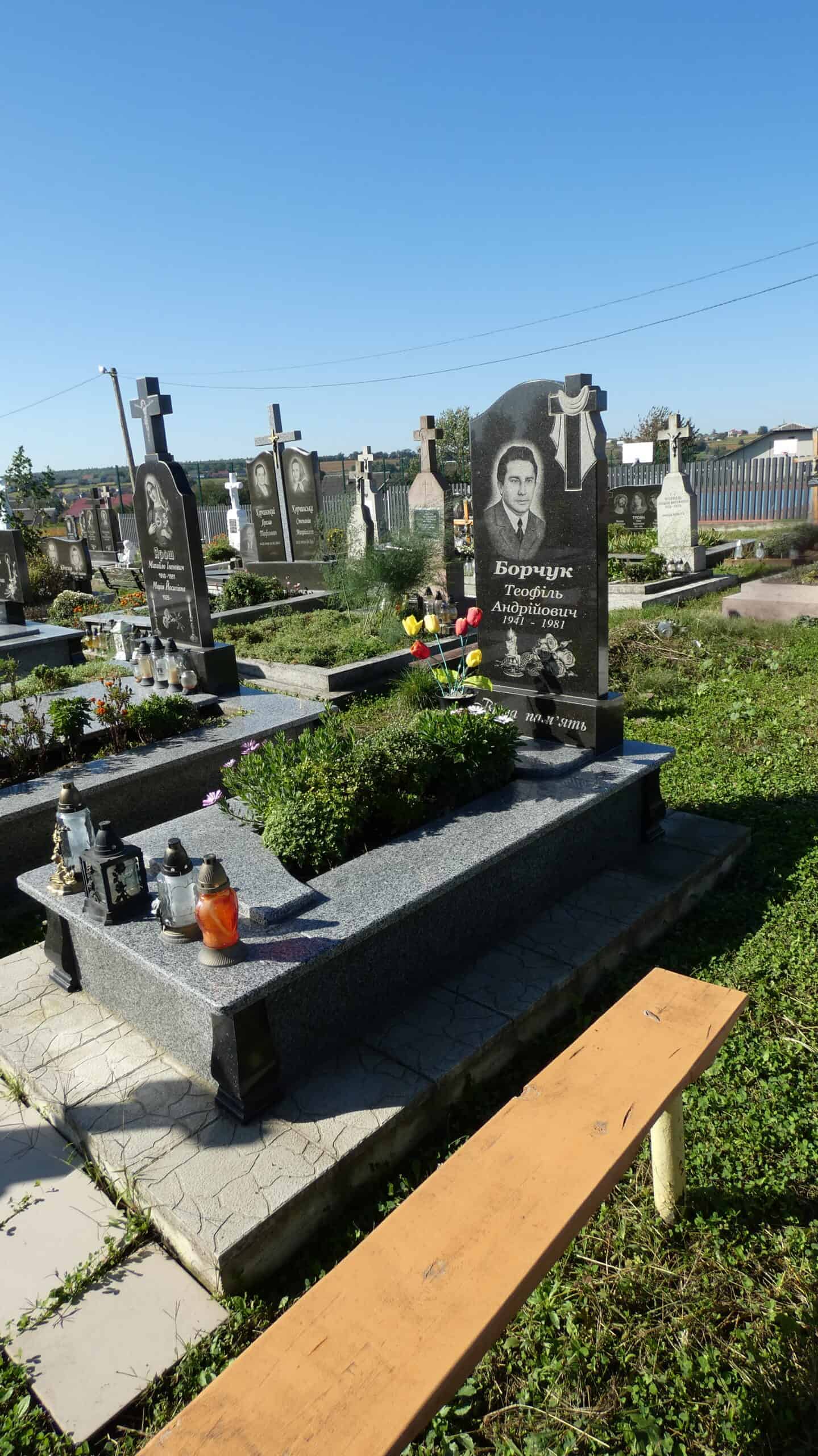Могила з портретом і пам’ятною таблицею, оздоблена квітами та лампадами.