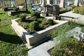 Могила з зеленими кущами та квітами на цвинтарі, пам'ятник і освітлення біля нас поховання.