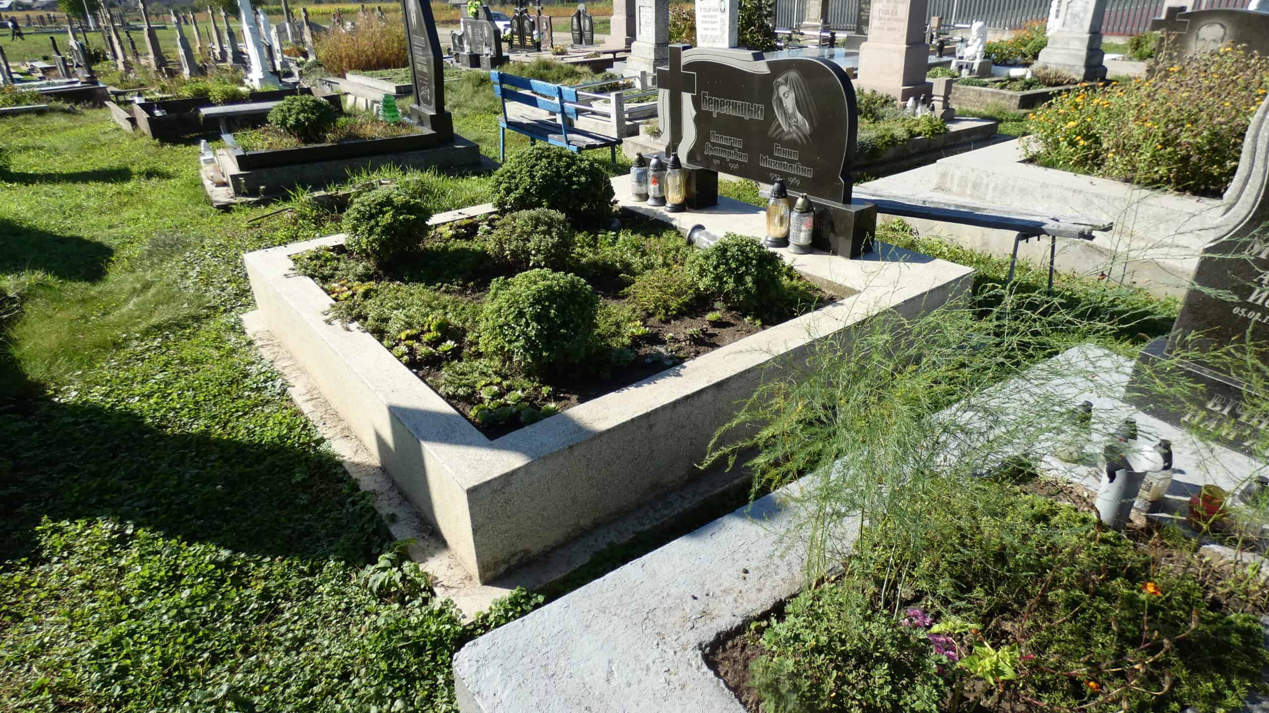 Могила з зеленими кущами та квітами на цвинтарі, пам'ятник і освітлення біля нас поховання.