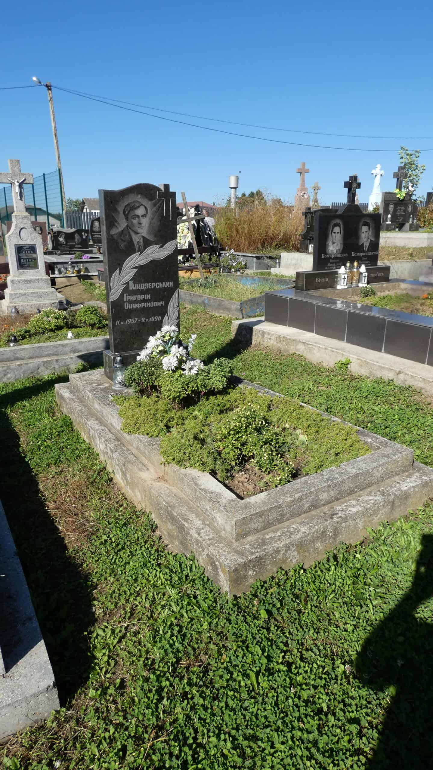 Могила з чорним пам’ятником та квітами на цвинтарі Букачівці, відкритий простір.