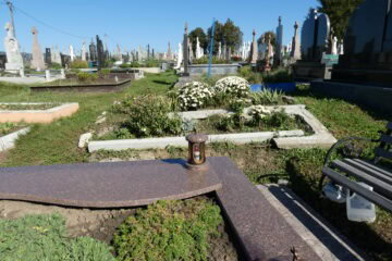 Могила на цвинтарі з квітами та лампадкою, історичне кладовище з похованнями та меморіалами.