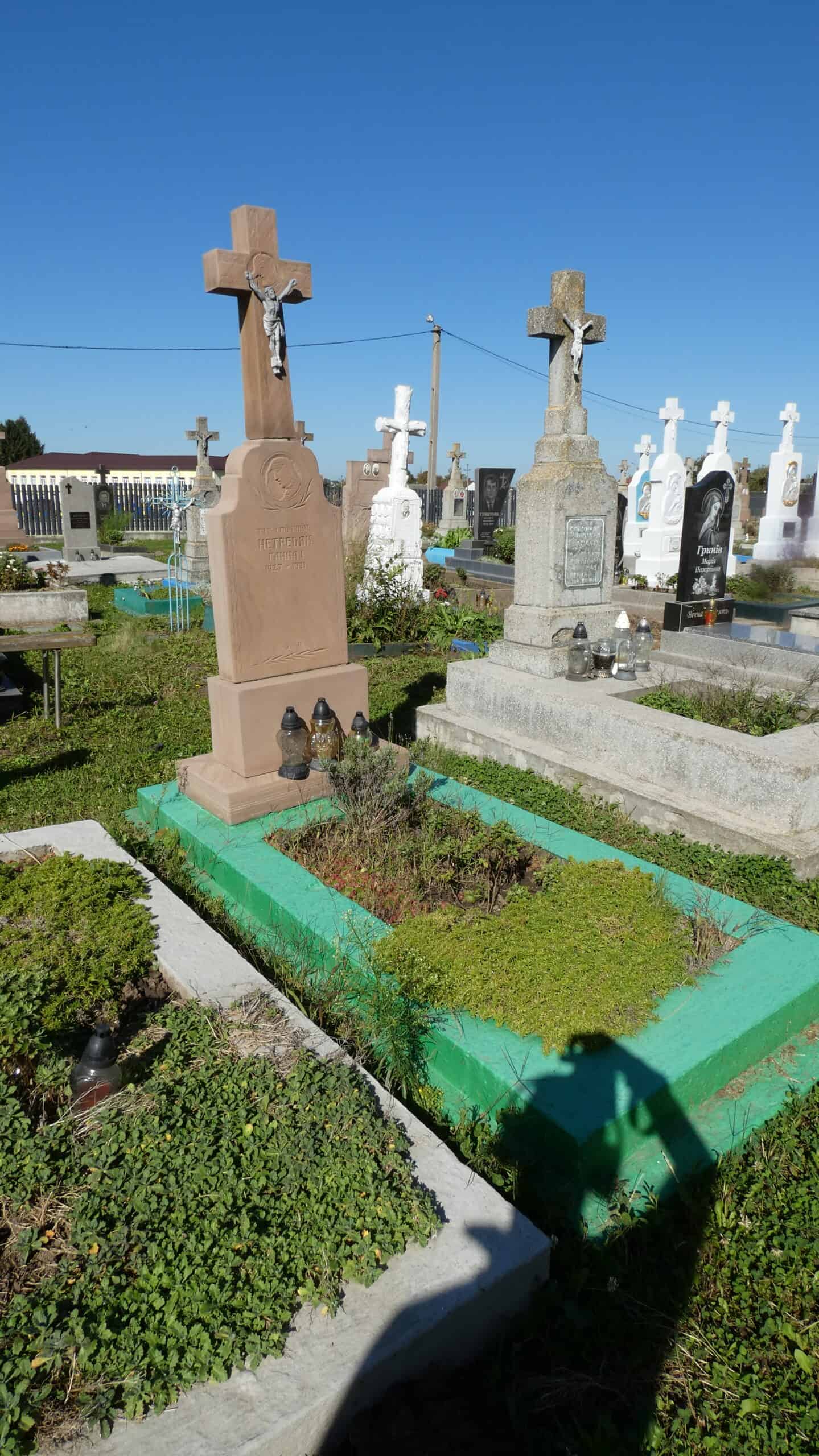 Меморіальний хрест на цвинтарі в Буцазі, могили з пам'ятними надгробками та квітами.