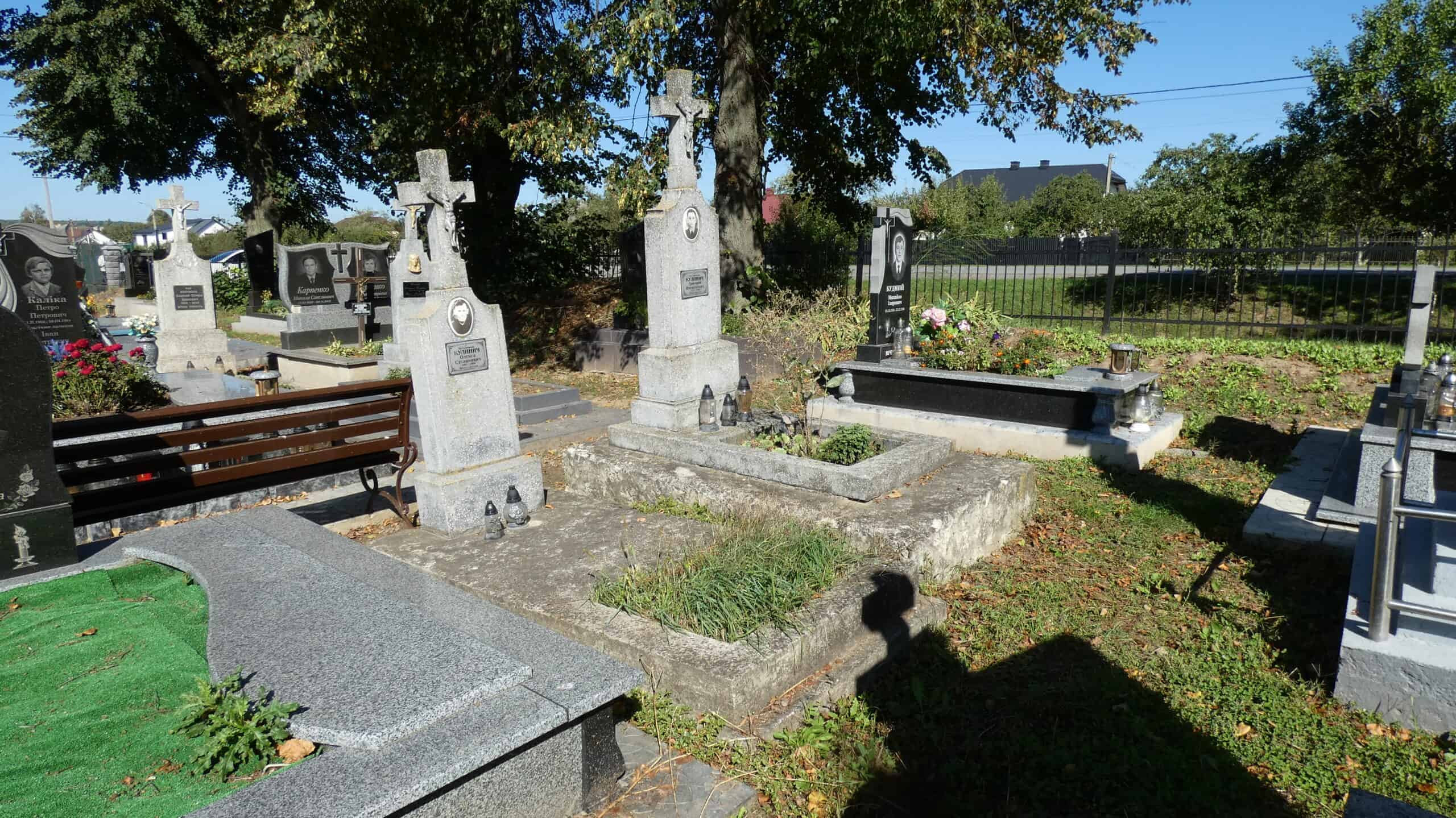 Меморіальні надгробки на старому цвинтарі Буцачі, могили з хрестами та квітами у яскравий сонячний день.