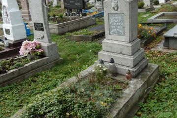 Вигляд могили на цвинтарі, пам’ятник з хрестом та фото померлого, квіткові та свічкові прикраси.