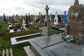 Могила з пам'ятником із хрестом та фотографіями родини, цвинтар у Буцьках, велика кількість поховань, квіти та лампадки.