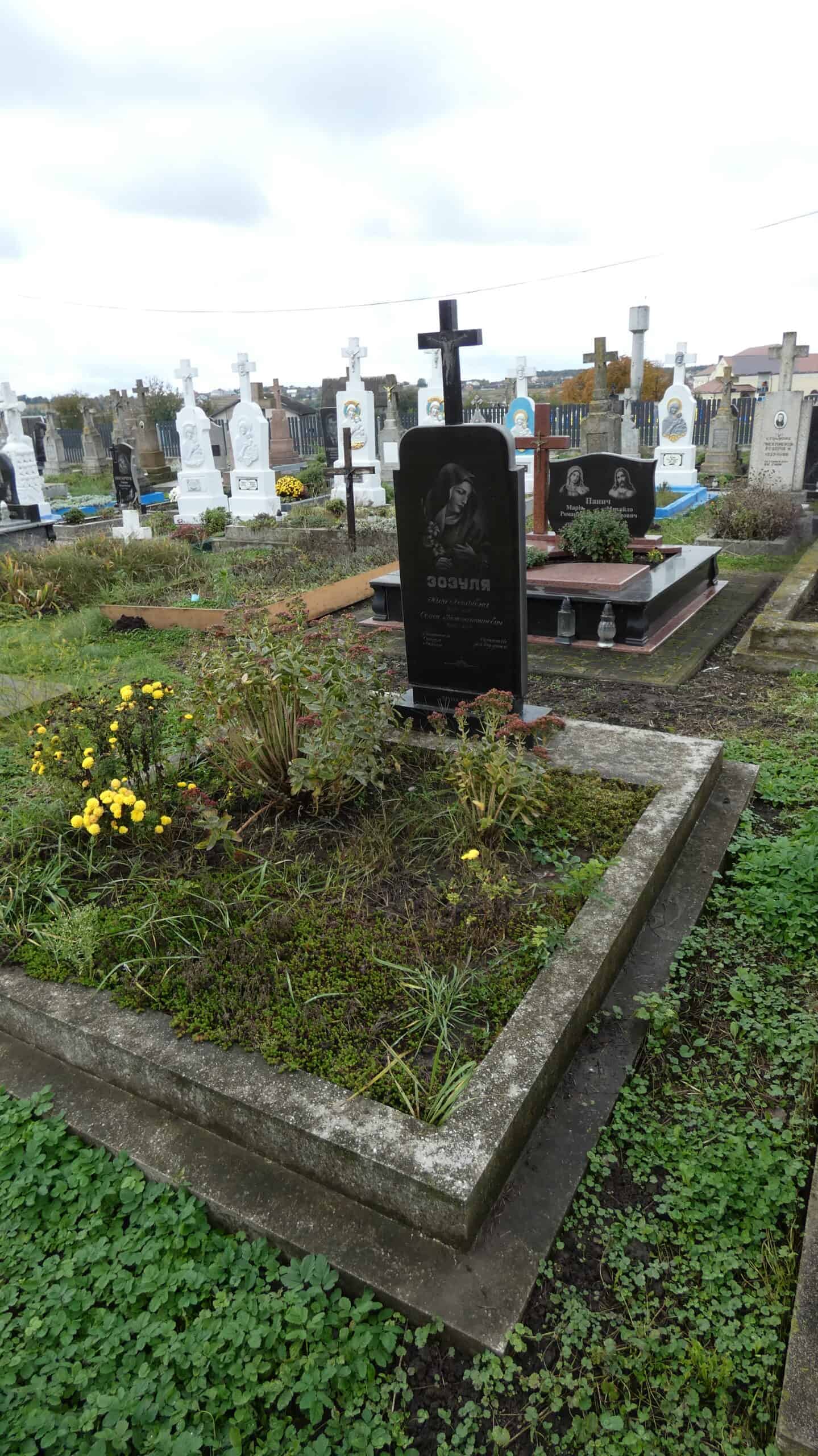 Могила з чорним пам’ятником і квітами у цвинтарі Буцач.