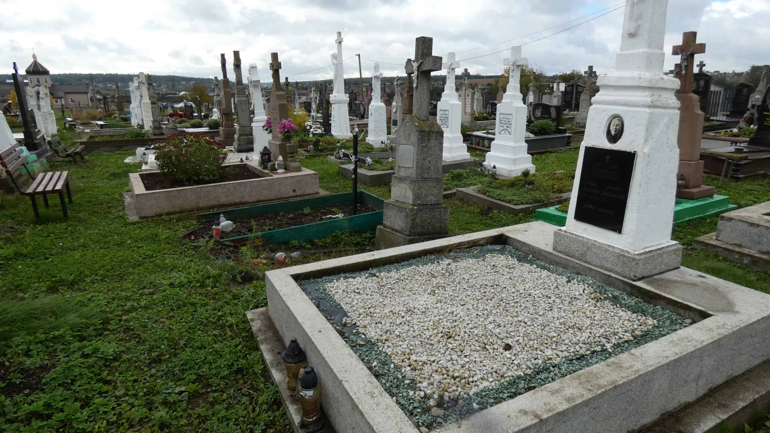 Могили на цвинтарі в Буцачі, могили з хрестами та пам'ятниками, чорний граніт-стела, похоронні пам'ятки в українському стилі.