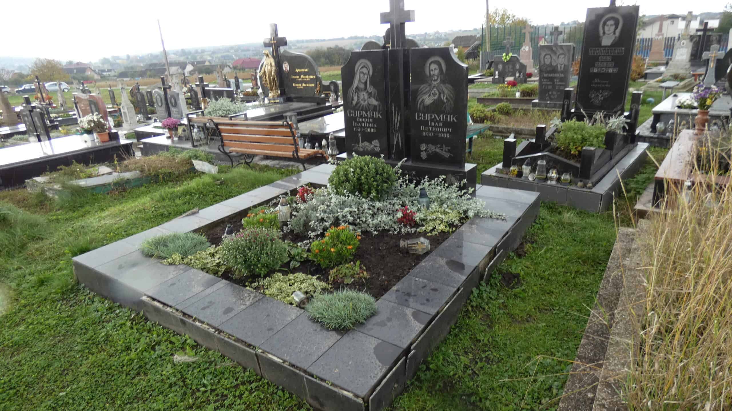 Захоронення на цвинтарі у Буцачі, сучасний могильний пам'ятник із квітами та огорожею.