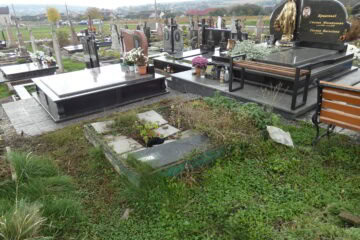 Білий та чорний надмогильний пам'ятник на цвинтарі у Буцачі, з квітами та лампадками, огороджений металевим парканом.