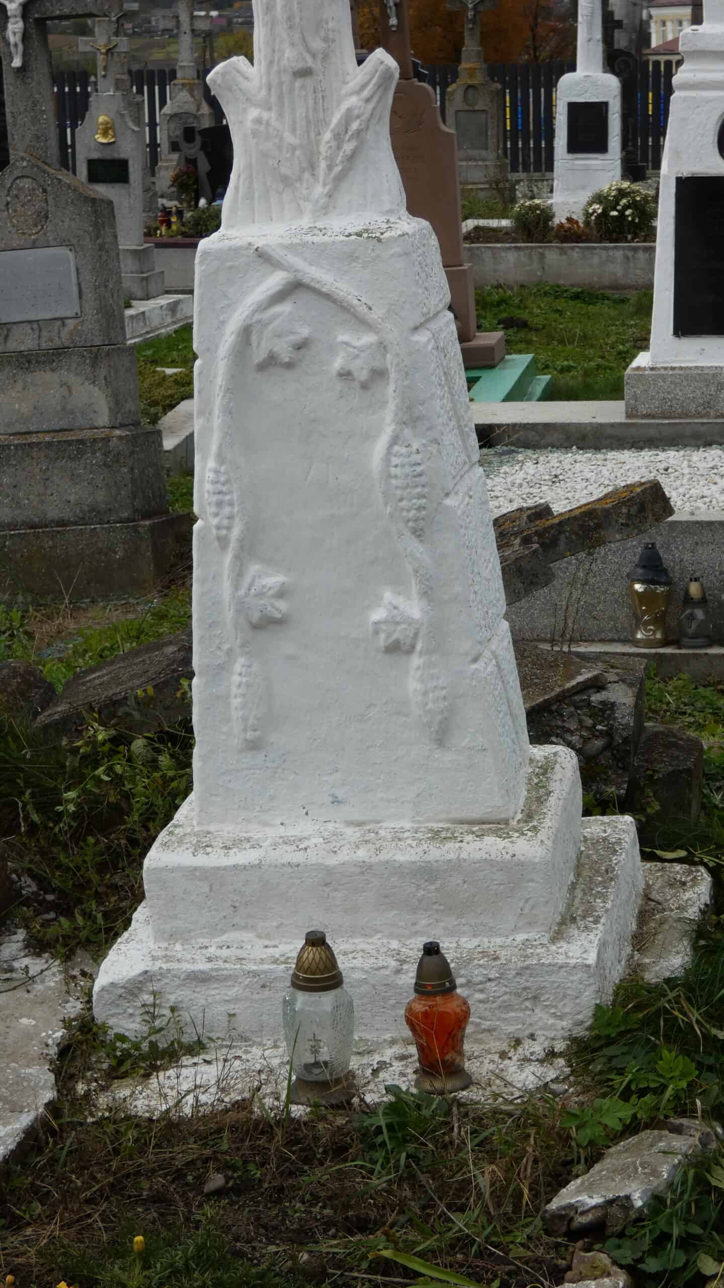 Вузький гранітний пам'ятник на цвинтарі з іконографікою, квітами та лампадами, символ пам'яті та вшанування.