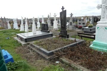 Могила на цвинтарі з різними пам'ятниками, хрестами та квітами, поховальні споруди, декор та пам’ятники на кладовищі.