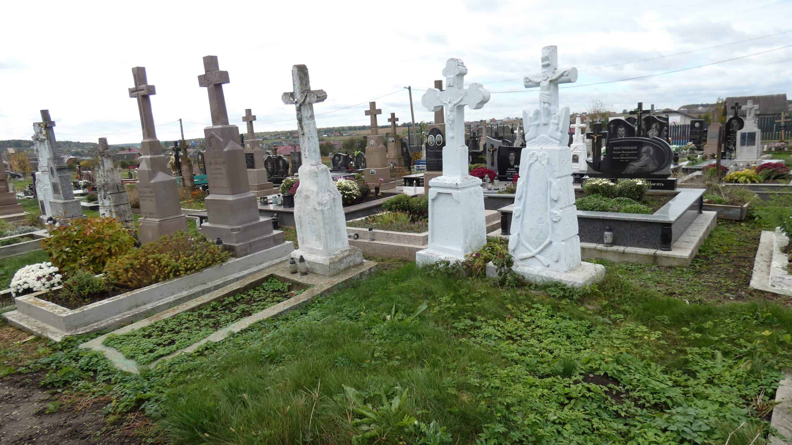 Могили на цвинтарі у Букачачі з хрестами та квітковими композиціями, меморіальні плити.