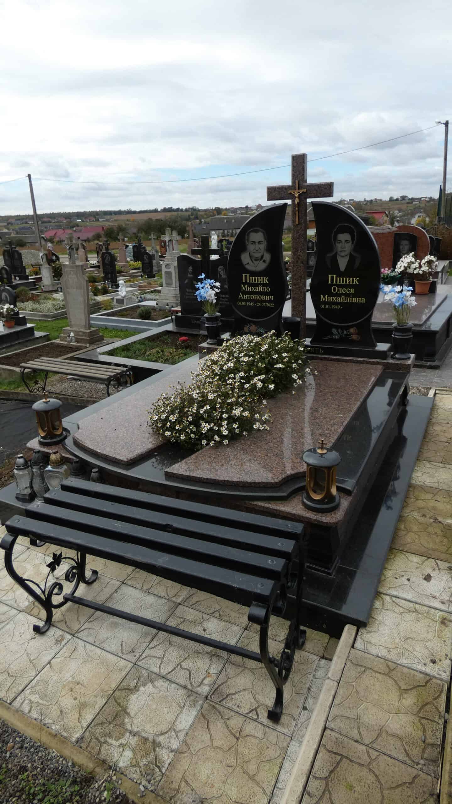 Меморіальний пам'ятник на цвинтарі, гранитний хрест та могила з квітами, укриття з каменю.