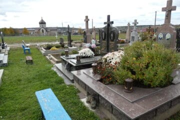 Могили на цвинтарі, панорамний огляд могил та пам’ятників, квіти і освітлювальні лампи.